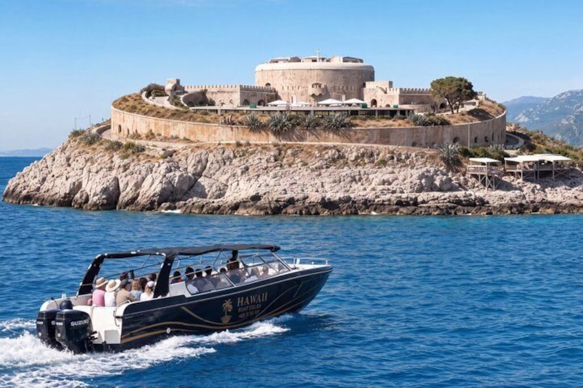 Un bateau nommé « Hawaii » sur l’eau, une île rocheuse surmontée d’une structure ressemblant à un château, et un ciel bleu dégagé. 3
