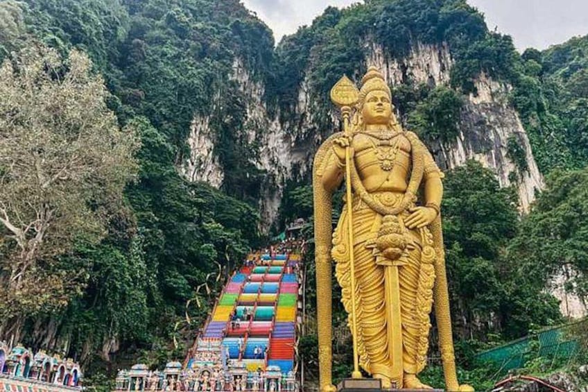 A large golden statue of a deity with a colorful staircase in a mountainous area. 1