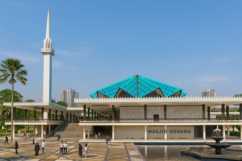 A mosque with a tall minaret and a turquoise roof, surrounded by a spacious courtyard with palm trees and a fountain. 4