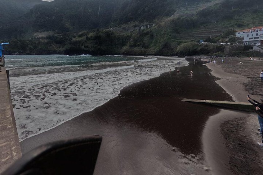 A beach with waves, a wooden boat, and a person standing on the shore. 2