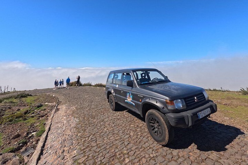 En bil parkeret på en brostensbelagt sti, med en gruppe mennesker i baggrunden. 3