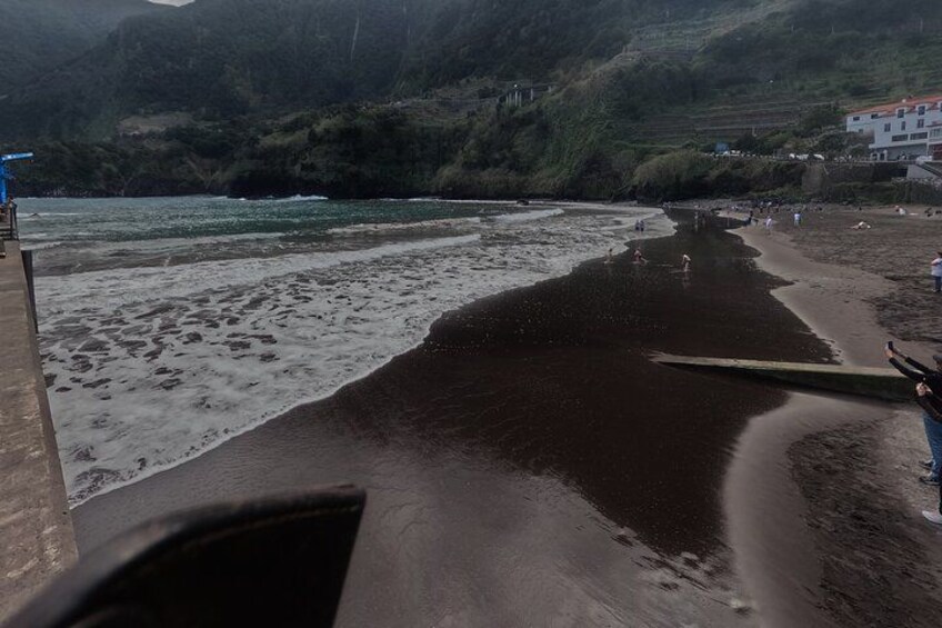 Una playa con olas, una estructura de madera y una colina al fondo. 3