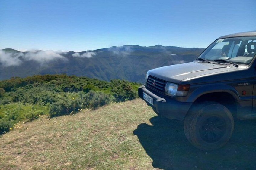 Ein Fahrzeug auf einer grasbewachsenen Anhöhe, im Hintergrund eine Berglandschaft. 4