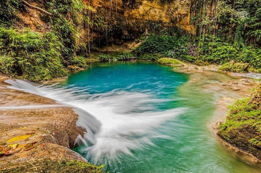 Ein türkisfarbener Fluss fließt durch ein bewaldetes Gebiet mit einem Wasserfall. 2