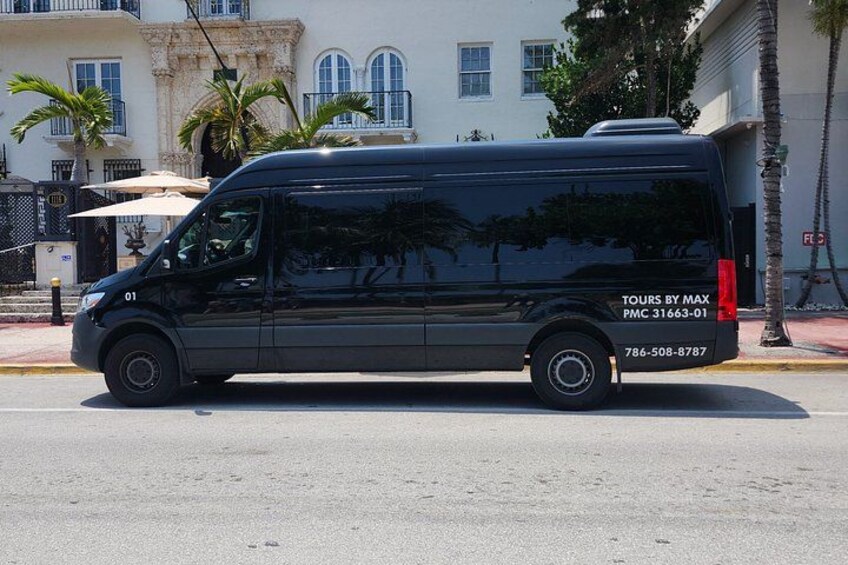 A black van parked on a street with palm trees and a building in the background. 4