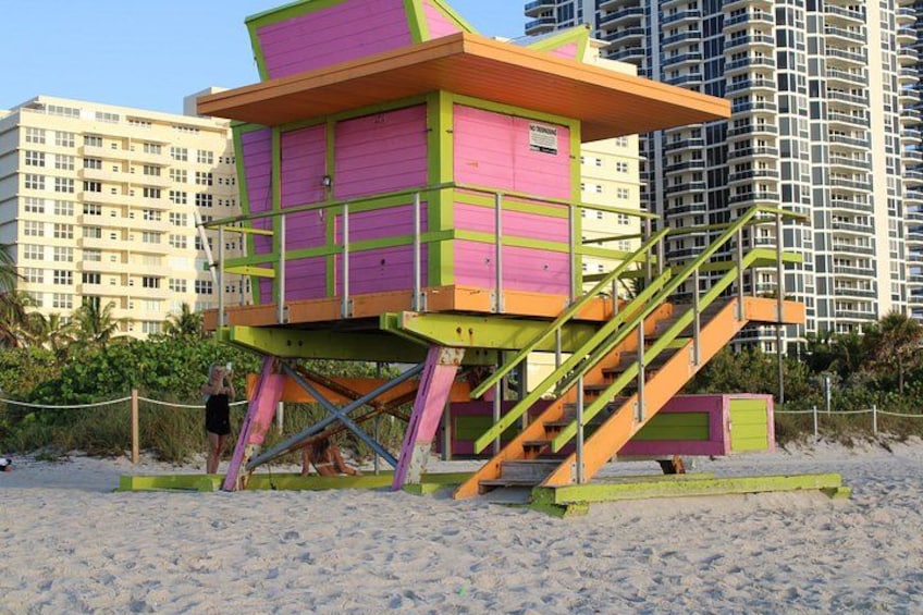 A colorful lifeguard tower on a sandy beach with a cityscape in the background. 2