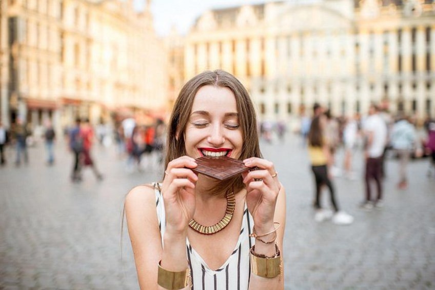 Una persona tiene una barretta di cioccolato in una piazza cittadina con edifici storici sullo sfondo. 3