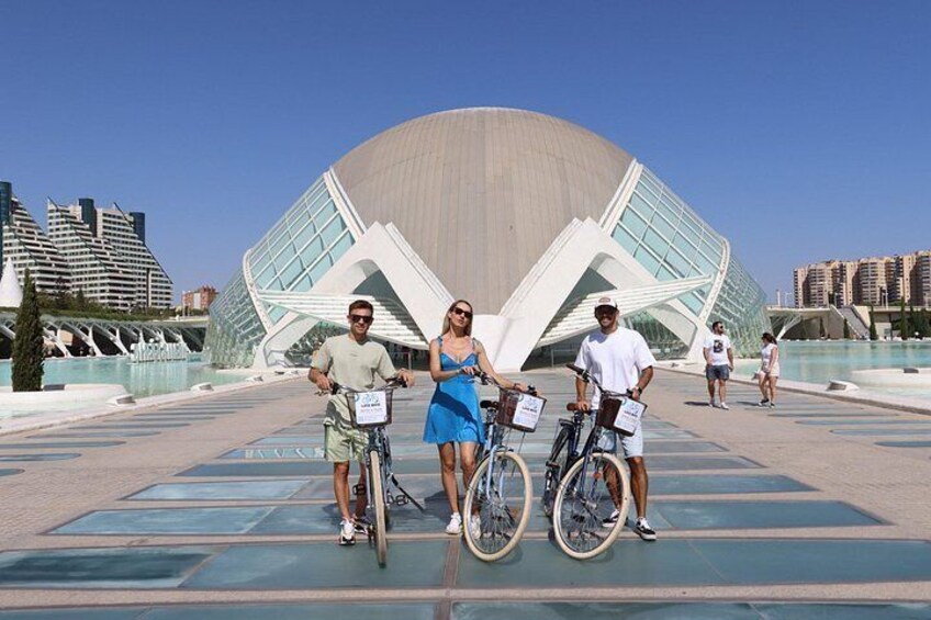Three people on bicycles in front of a modern architectural building. 3