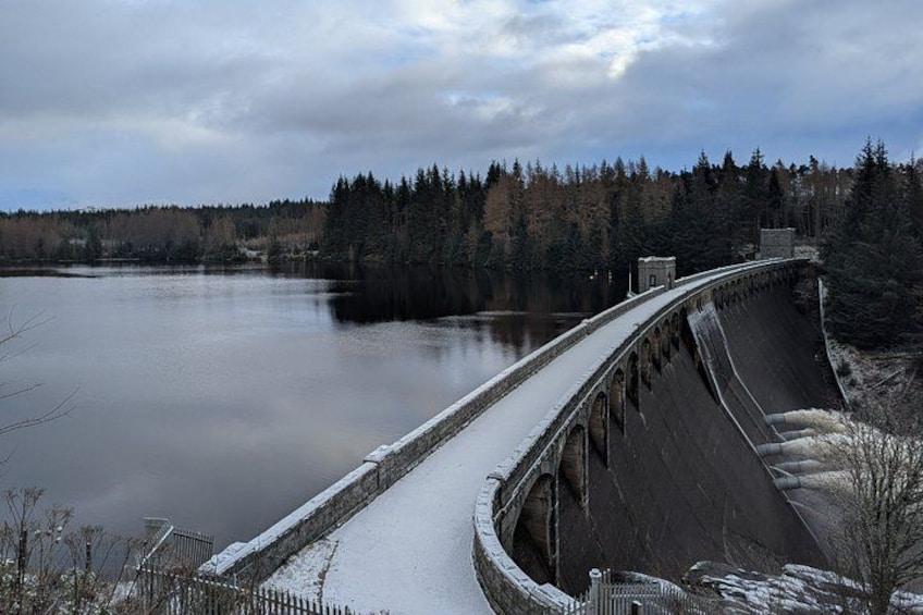 Ein Stausee mit einem verschneiten Weg, einem ruhigen See und bewaldeter Landschaft im Hintergrund. 3