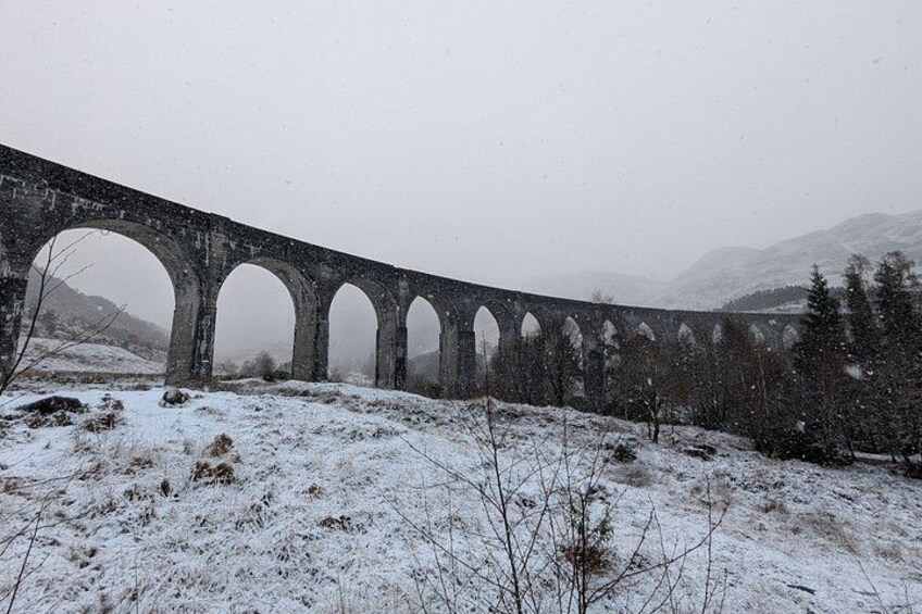 Ein mit Schnee bedeckter Viadukt mit mehreren Bögen, umgeben von verschneiter Landschaft und Bäumen. 2