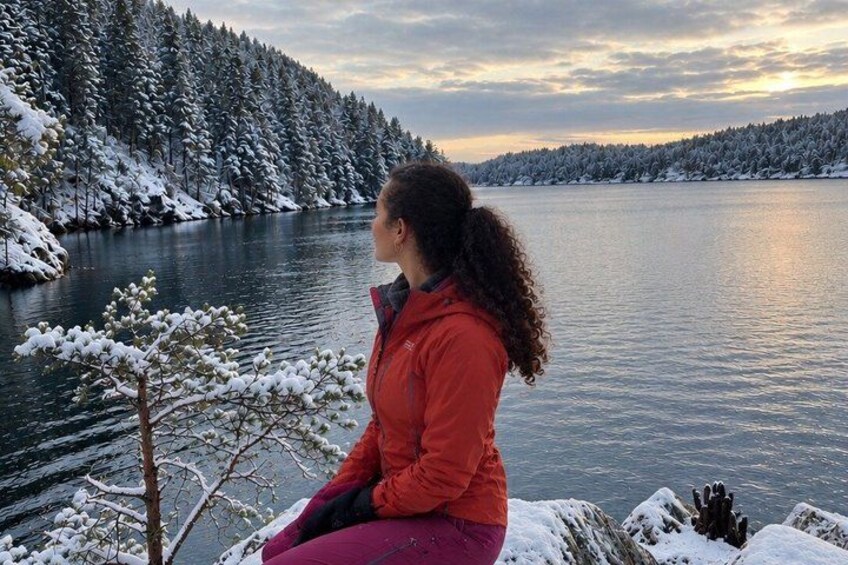 A person sitting by a snow-covered lake with trees in the background. 3