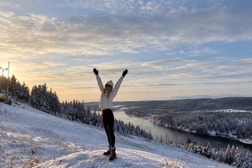 A person standing on a snow-covered slope with arms raised, overlooking a river and forested landscape. 5