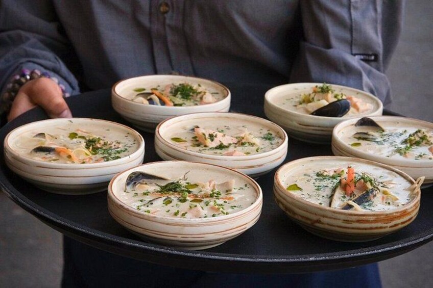 A person holding a tray with multiple bowls of seafood soup. 3