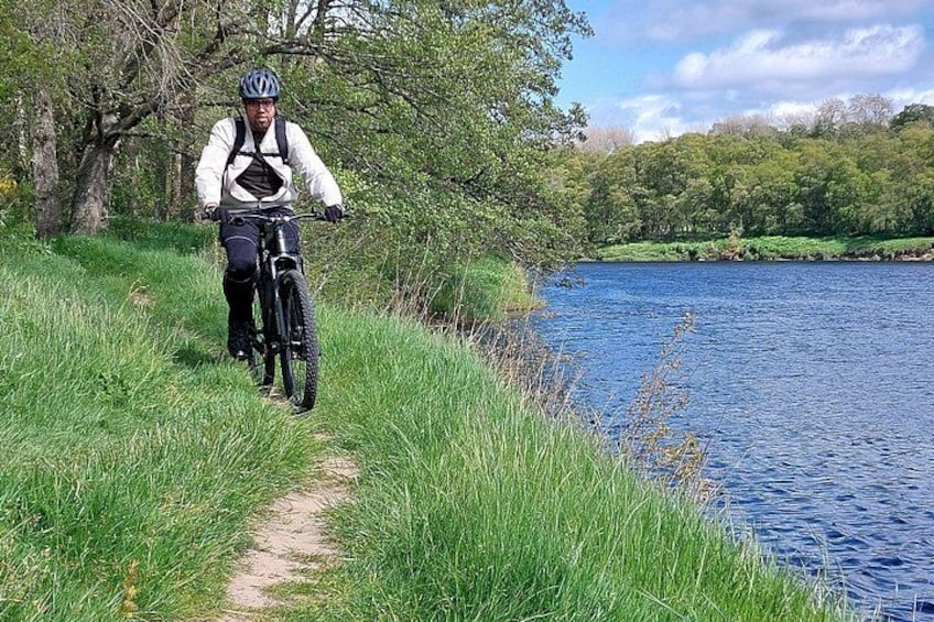 A person riding a mountain bike on a grassy path beside a body of water. 3