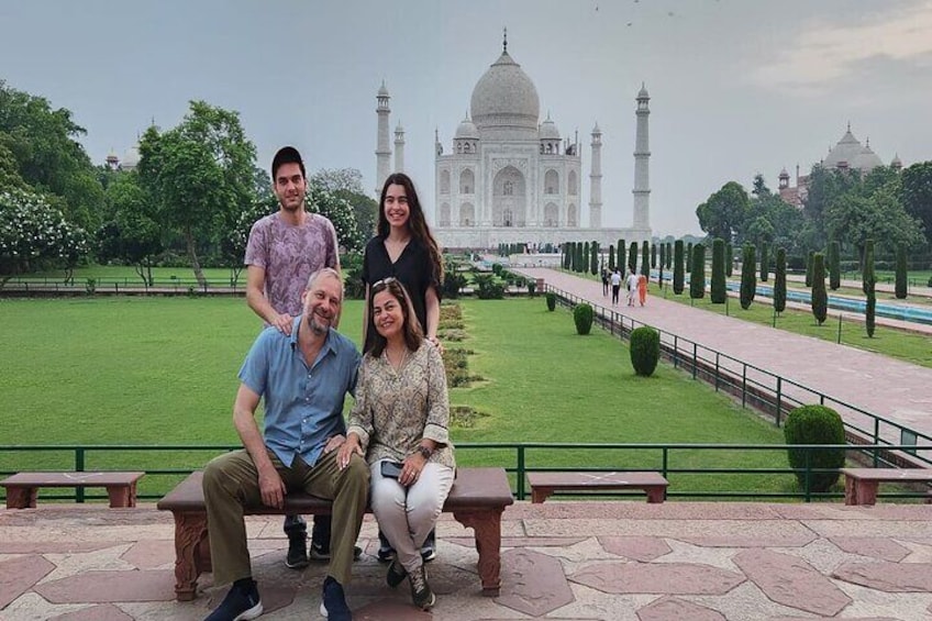 A group of people sitting on a bench with the Taj Mahal in the background. 1
