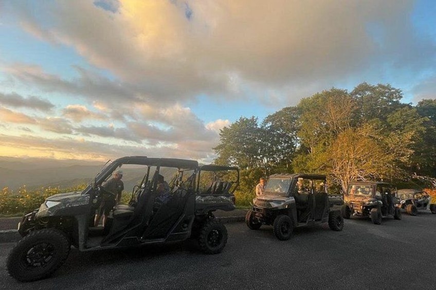 A line of off-road vehicles parked on a road with trees in the background. 3