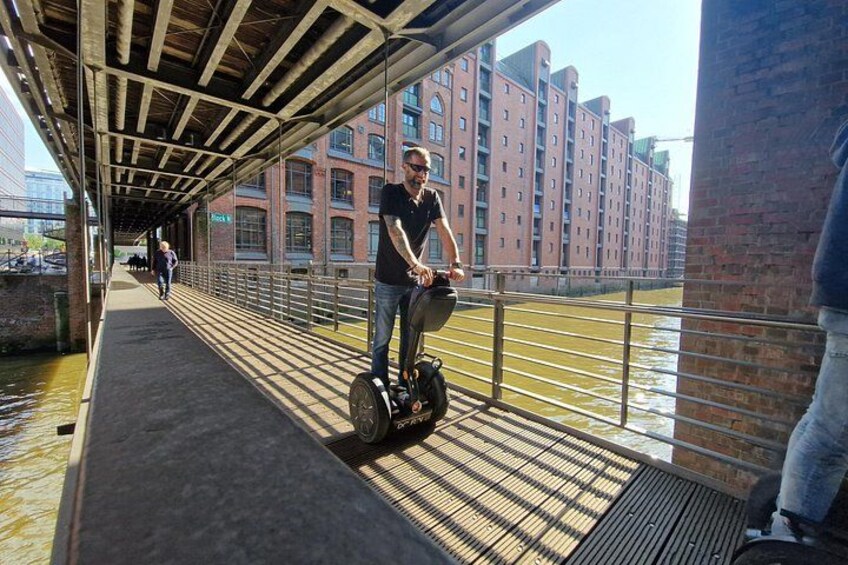 En person kører på en Segway på en fodgængerbro over en kanal, med bygninger i baggrunden. 2