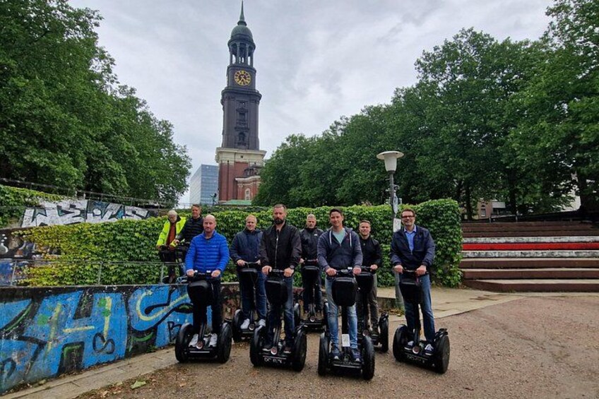 En gruppe mennesker på segways i en bypark med et klokketårn i baggrunden. 5