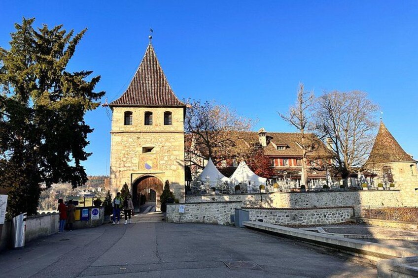 Ein historischer SteinTurm, eine Kirche mit einem spitzenTurmdach und eine Steinmauer mit einem Tor. 3