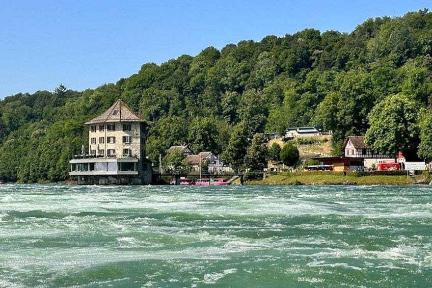 Ein Fluss mit einem Haus auf Stelzen, umgeben von üppigen grünen Hügeln. 5