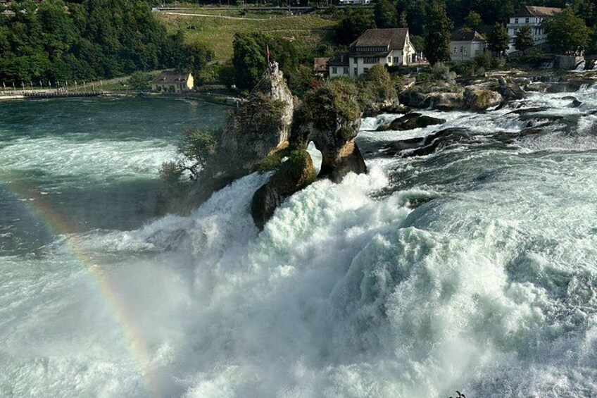 Ein Fluss mit einem Wasserfall, einem Regenbogen und Häusern im Hintergrund. 4