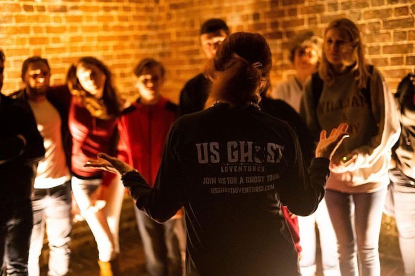 Un grupo de personas en una habitación de ladrillo con poca luz, algunas vestidas con chaquetas que llevan texto en la parte de atrás. 3