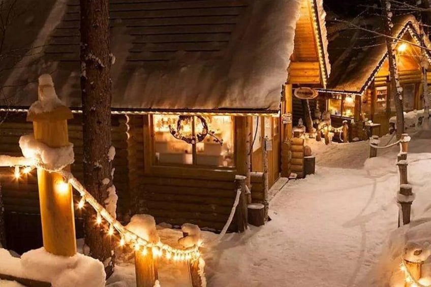 A snow-covered wooden cabin with string lights and a snow-covered path. 2