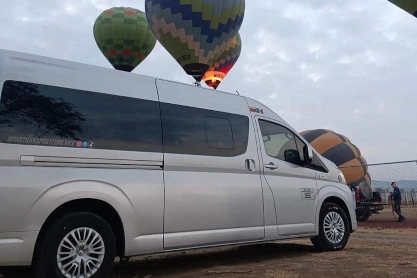 A white van parked with hot air balloons in the background. 5