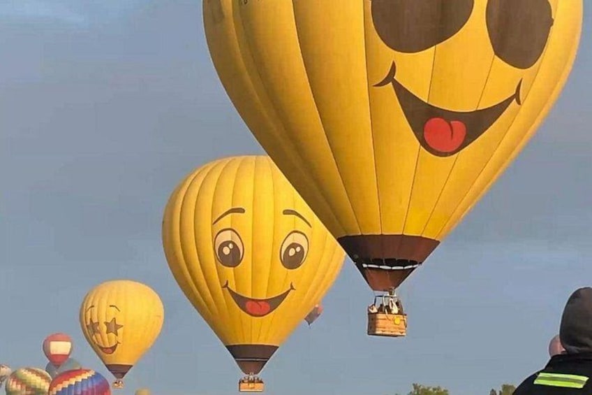 A group of hot air balloons with faces, including a smiling face and a starry face, against a clear sky. 4