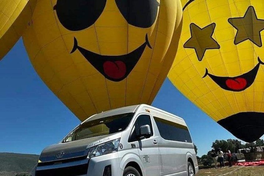 A white van parked under large yellow hot air balloons with smiley faces. 3