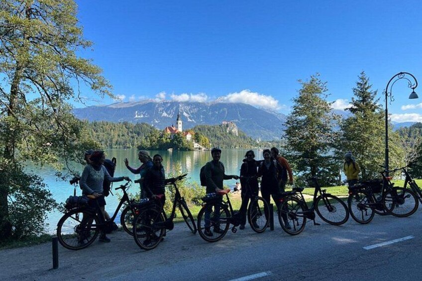 Un grupo de ciclistas en un camino pavimentado, con un lago y montañas al fondo. 3