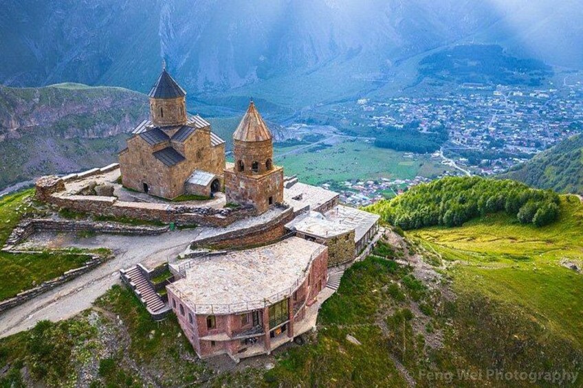 A historic church complex with multiple domes, surrounded by mountainous terrain and a valley below. 4