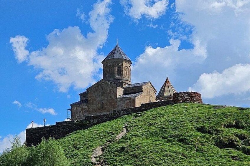 A historic stone building with a bell tower on a hill, surrounded by greenery. 3