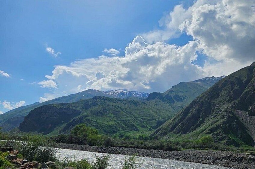 A river flowing through a mountainous landscape with green hills and a clear sky. 2