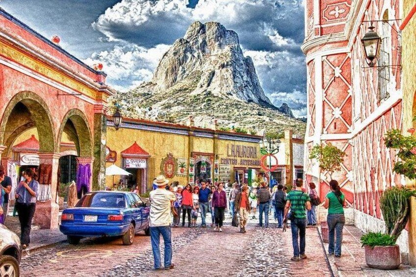 A cobblestone street with people, a blue car, and a mountain in the background. 5