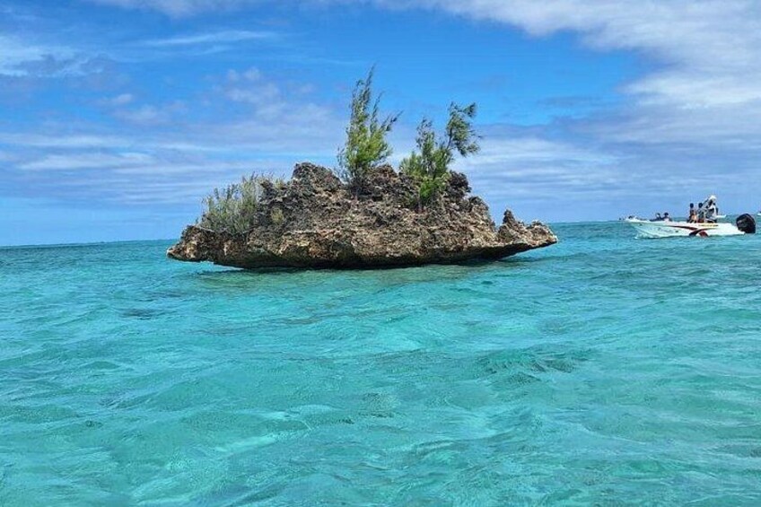 A small rocky island surrounded by clear turquoise water, with a boat visible in the distance. 3