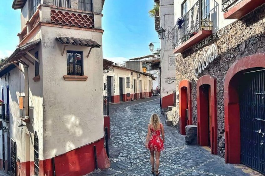 A woman in a red dress walking down a cobblestone street in a historic town. 3
