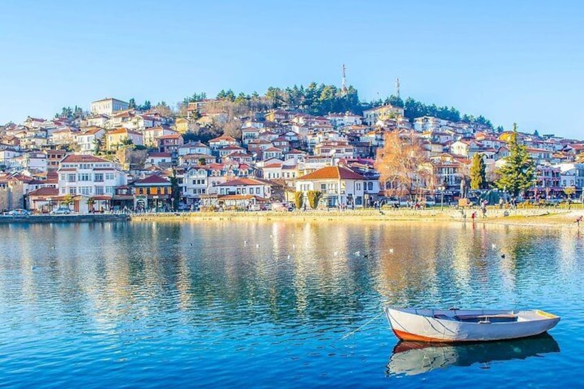 Un lago calmo con una barca, una cittadina arroccata su un pendio e un cielo azzurro terso. 2