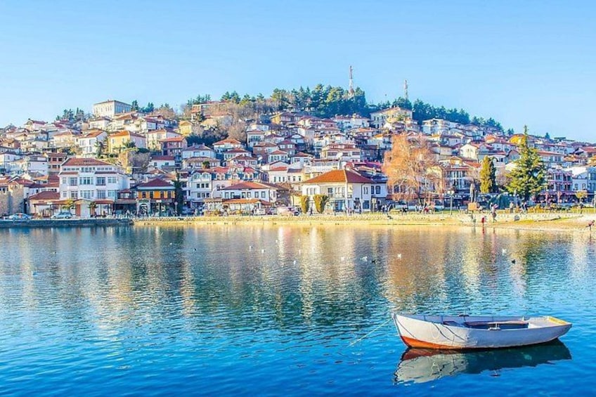 Un lac paisible avec un bateau, une ville perchée sur une colline densément peuplée et un ciel dégagé. 2