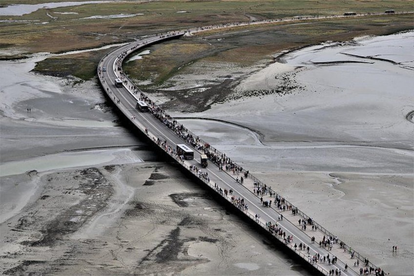 A bridge over a dry riverbed with a crowd of people and vehicles. 3