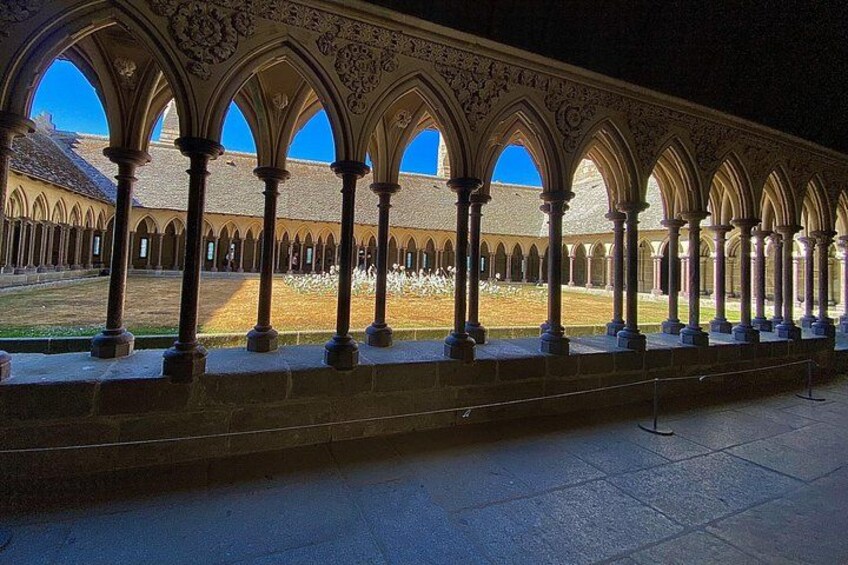 A cloister with arched walkways and columns, a courtyard, and a building with a sloped roof in the background. 4