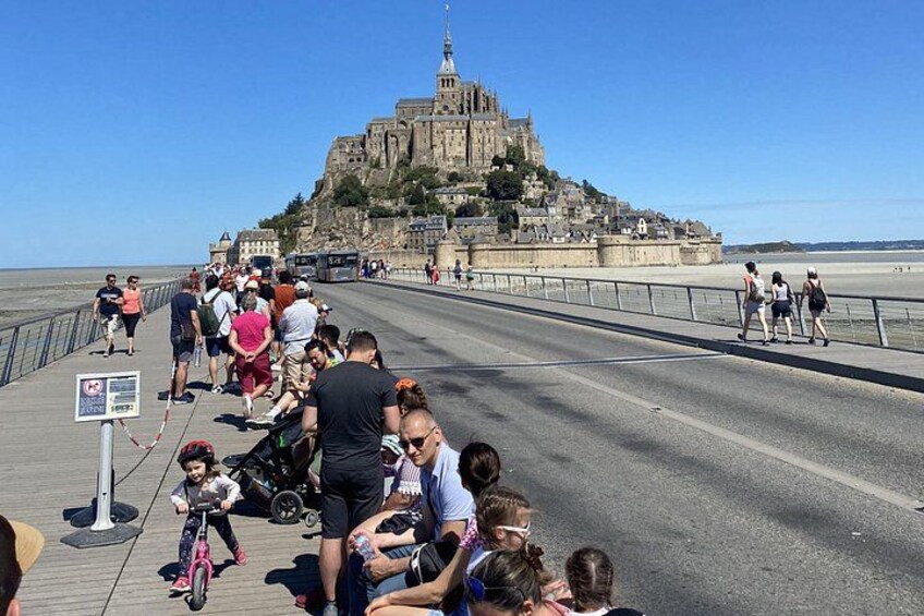 A crowded promenade with people walking and cycling, overlooking a historic castle on a hill. 2