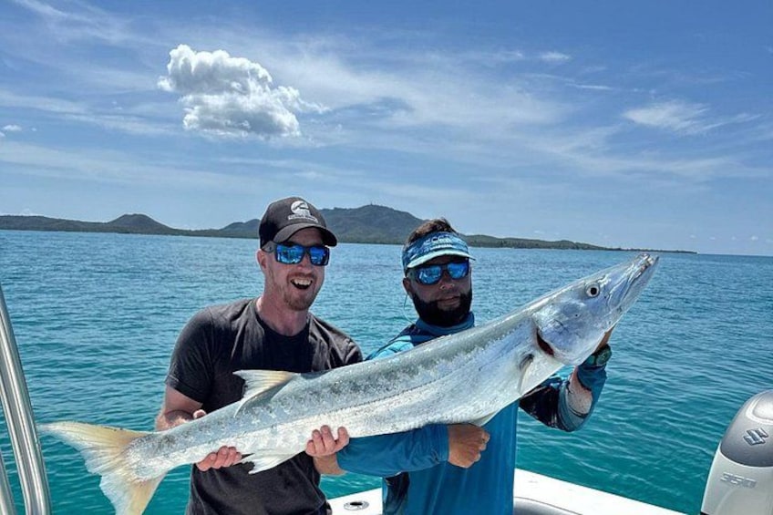 Two people holding a large fish on a boat with a clear sky and water in the background. 4