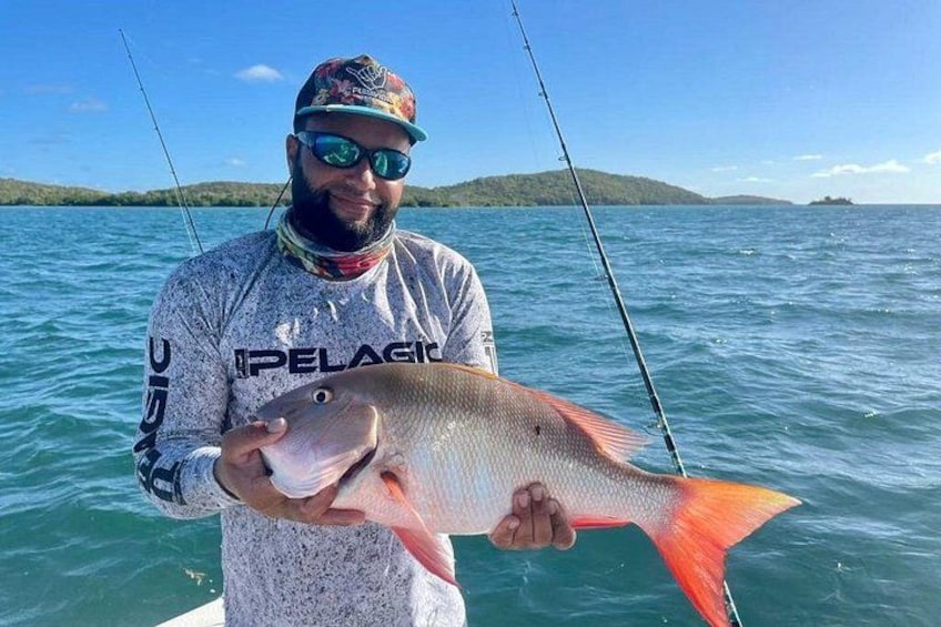A person holding a fish with a fishing rod in a body of water with a distant landmass. 1