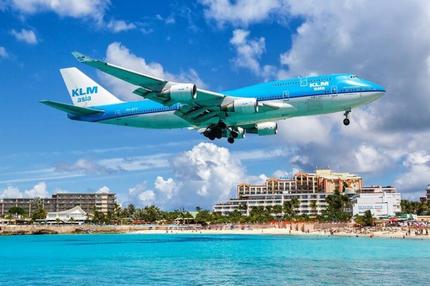 Ett KLM-flygplan på väg över ett område i Asien, med en strand och byggnader i bakgrunden. 1