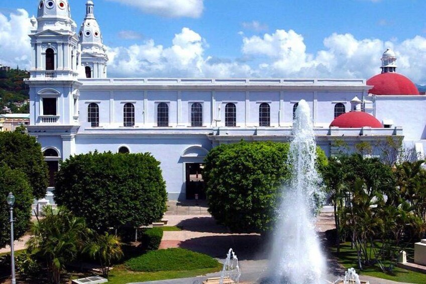 Un edificio blanco con cúpulas rojas, una fuente y abundante vegetación. 5