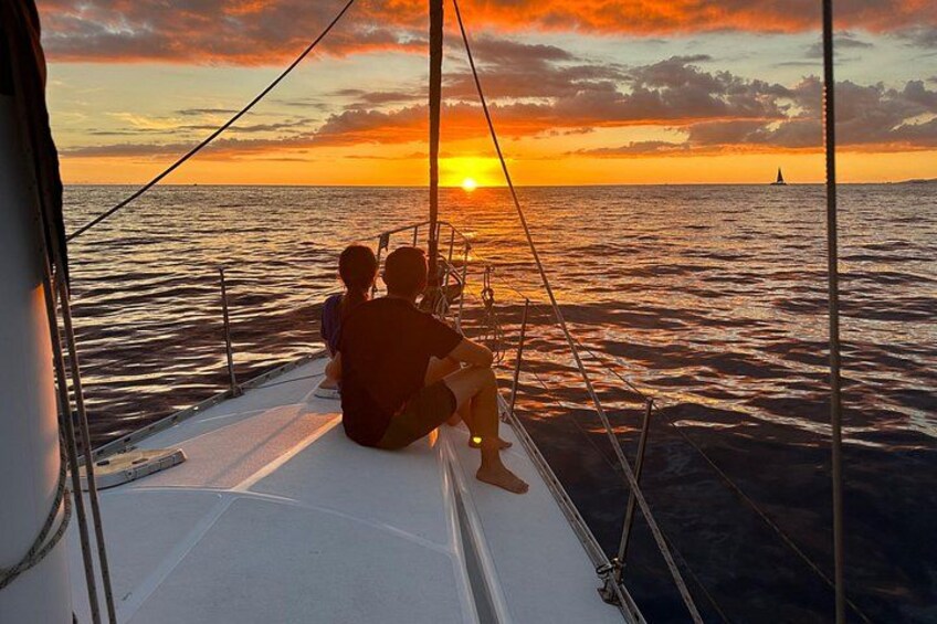 En solnedgång över havet med en segelbåt och två personer som sitter på däck. 4