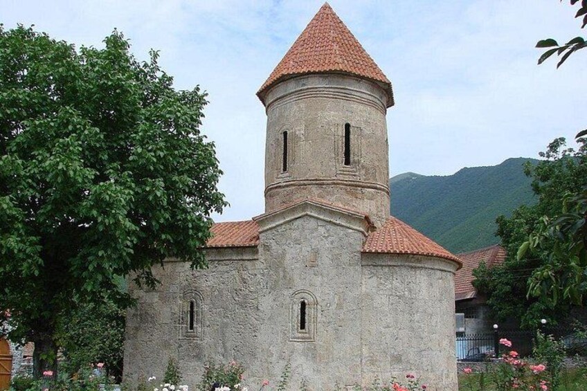 A stone church with a red-tiled roof and a bell tower. 1