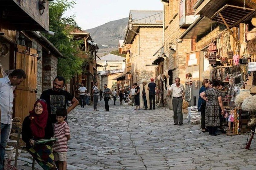 A cobblestone street in a historic town with people walking, shops on the sides, and a mountain in the background. 4