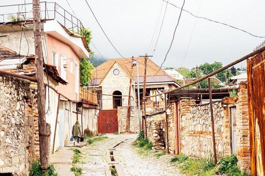 A narrow cobblestone street flanked by stone buildings, a red gate, and a wooden fence. 2